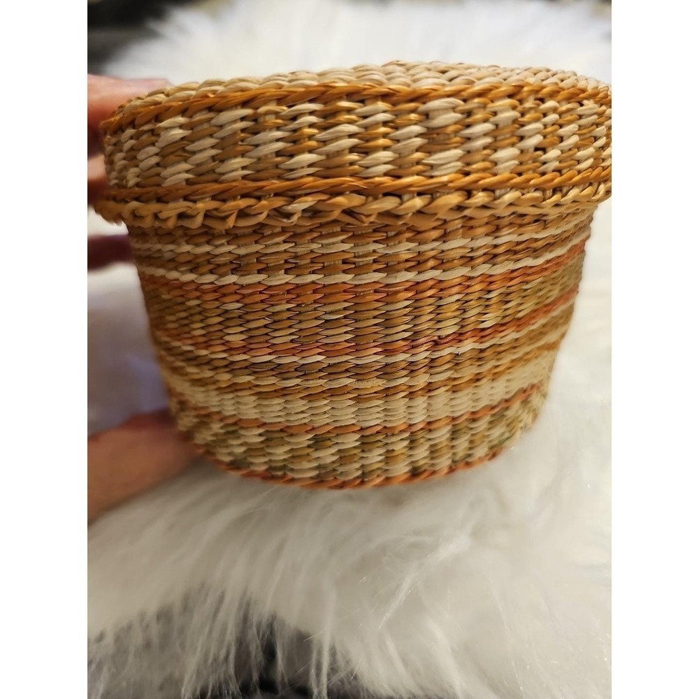 The image displays a‎ small, round, hand-woven basket with a lid, typically made